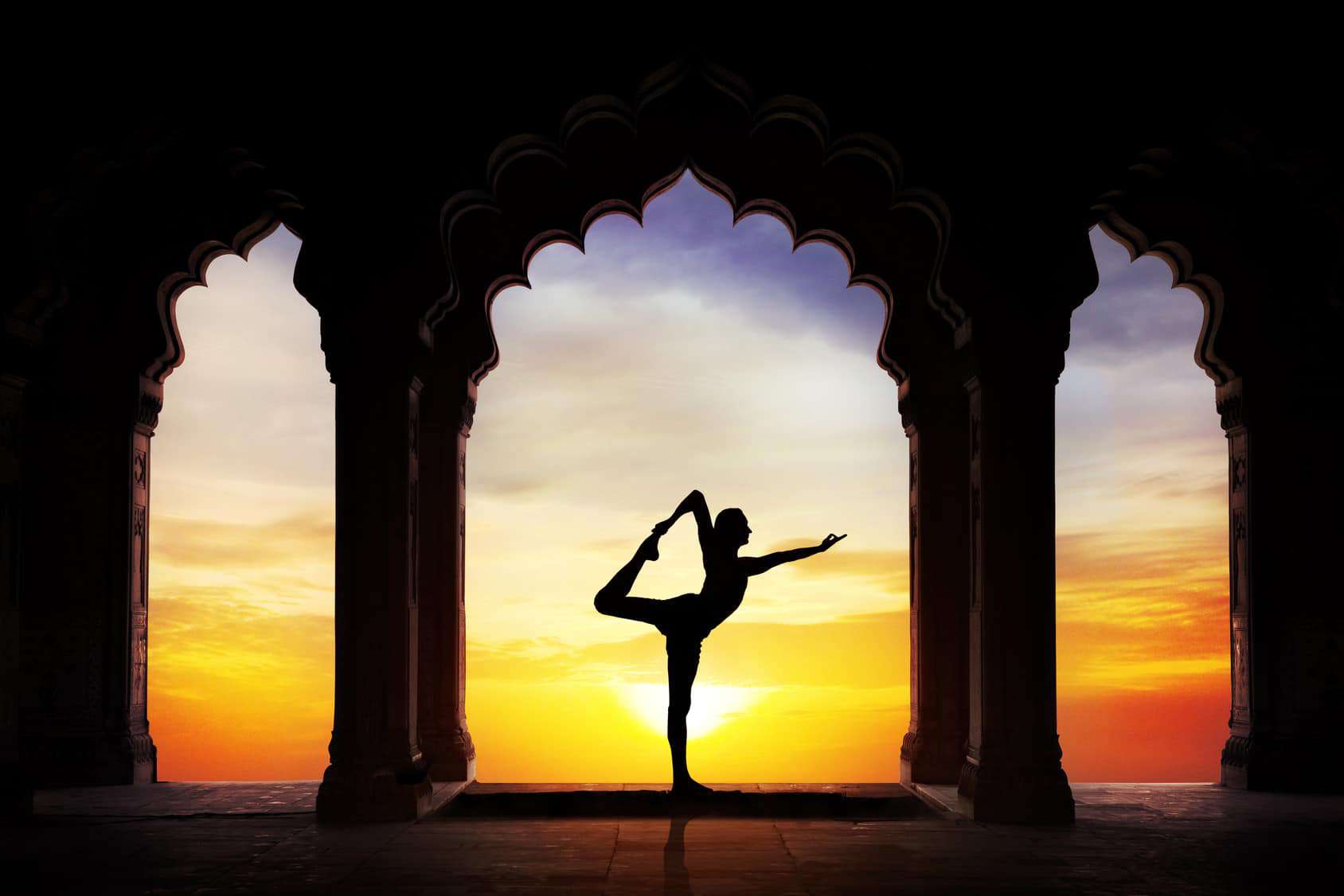 Silhouette qui pratique son yoga entre les colonnes d'une arche au coucher du soleil