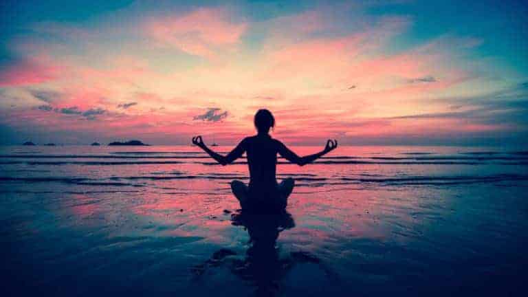 Silhouette d'une jeune femme qui pratique son yoga à la plage au coucher du soleil.