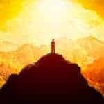 Silhouette d'une personne en haut d'une montagne, qui regarde le coucher de soleil.