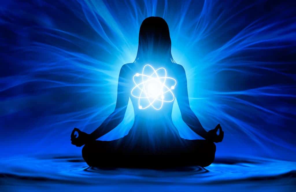 Une silhouette d'une personne en position du lotus méditant sur un fond bleu vif. Une lumière vive émane de leur poitrine, formant un symbole semblable à un atome avec des lignes d'énergie lumineuses s'étendant vers l'extérieur, créant un sentiment de spiritualité et de paix intérieure comme on pourrait percevoir une aura.