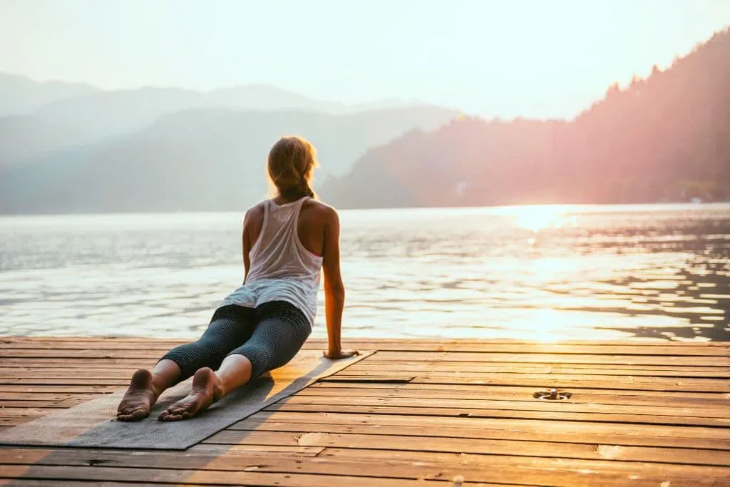 Une femme pratiquant le Kriya Yoga sur un quai près d'un lac.