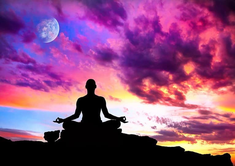 La silhouette d'une personne assise les jambes croisées dans une pose méditative, pratiquant l'Ishta Yoga sur une surface rocheuse. L’arrière-plan est un ciel vibrant et coloré au coucher du soleil avec des nuances de rose, de violet et d’orange. Une pleine lune est visible dans le coin supérieur gauche, partiellement obscurcie par les nuages, évoquant le mystique Rituel de la Lune.