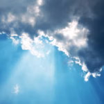 La lumière du soleil traverse les nuages sombres et épais sur fond de ciel bleu, créant des rayons de lumière saisissants. Ce spectacle céleste évoque le concept du plan astral, soulignant une atmosphère dramatique et d'un autre monde.