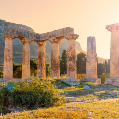 Sous un coucher de soleil doré, les anciennes colonnes du temple d'Apollon s'élèvent au milieu d'arbustes verts et d'une montagne en toile de fond - une scène évocatrice qui fait écho à la sagesse trouvée dans "Comment Édifier une Base Solide à Votre Chemin Spirituel".