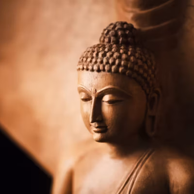 Gros plan sur une statue de Bouddha sereine, aux tons chauds de brun doré. Les yeux fermés et le regard serein, elle incarne le karma et la contemplation paisible. L'arrière-plan légèrement flou met en valeur le travail artisanal minutieux de la statue.