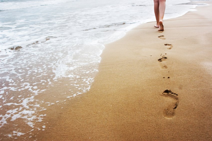 quelqu'un qui laisse ses traces de pas dans le sable, sur la plage au bord de l'eau